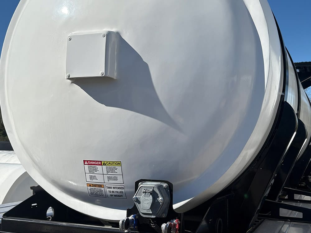 Food-grade tank trailer from Poly-Coat Systems showing the white tank head, fittings and safety labels.
